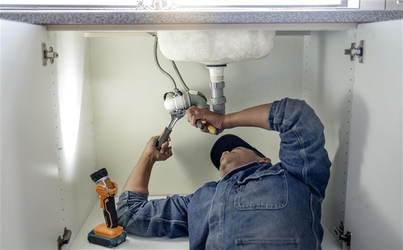 Plumber repairing pipes beneath a bathroom sink in Burlingame